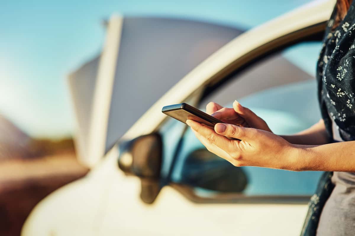 woman using phone on the side of the road with a broken down car
